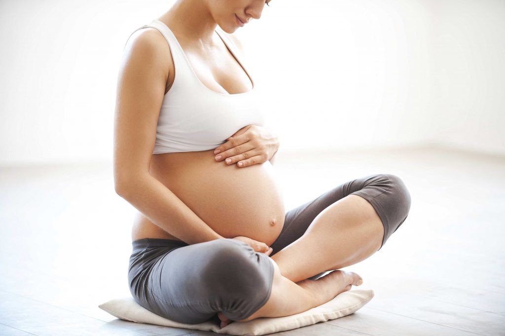 Waiting for a baby. Close-up of pregnant woman touching her belly while sitting in lotus position