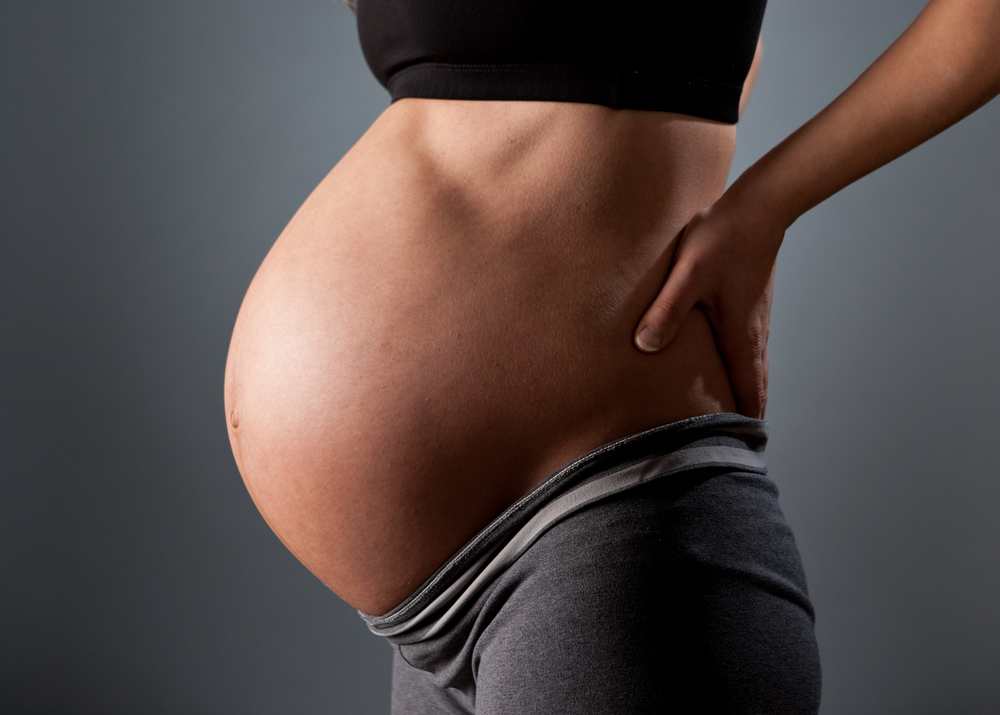 Waiting for a baby. Close-up of pregnant woman touching her belly while sitting in lotus position