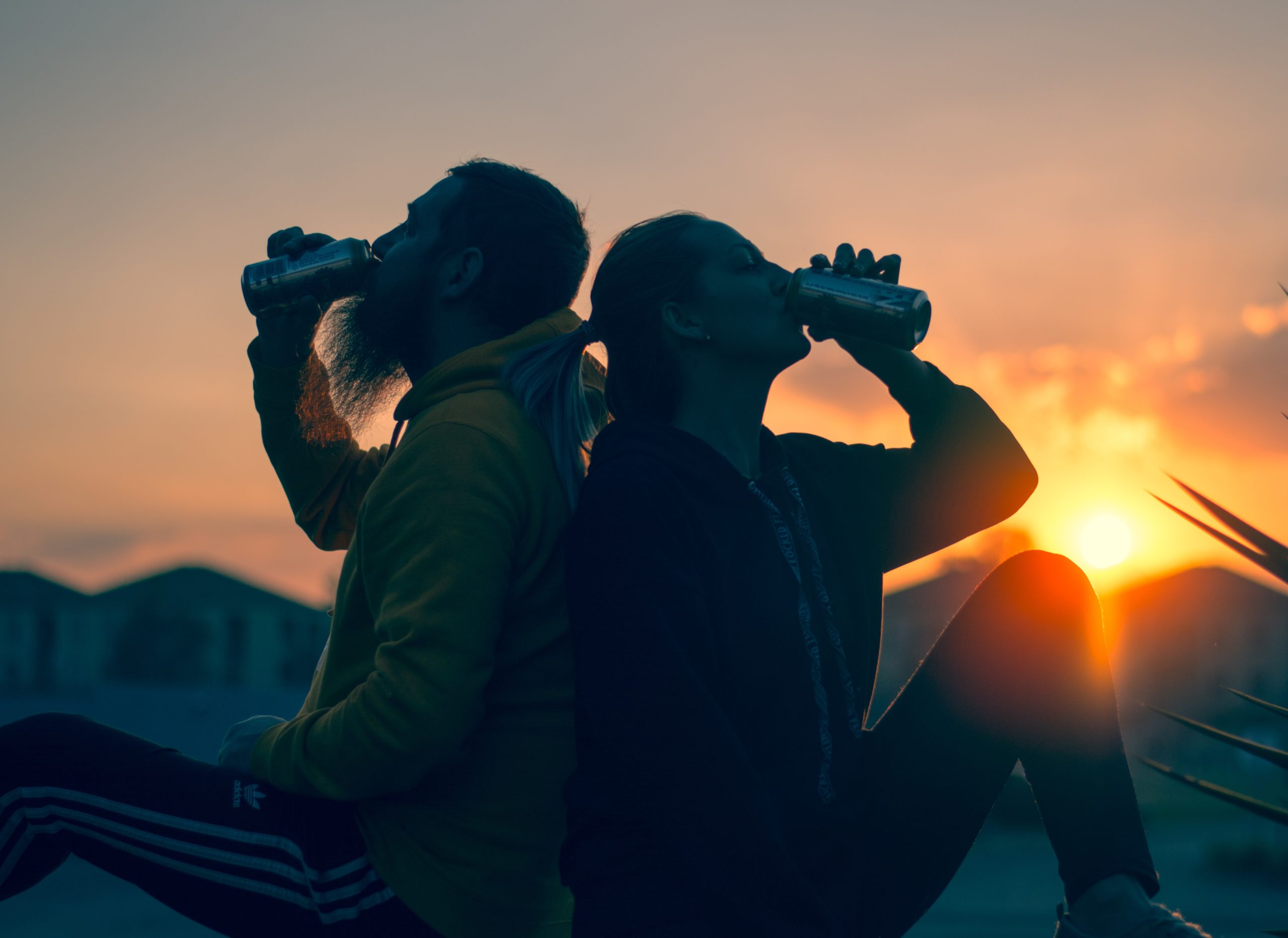 two young people drinking beer during while the sun goes down sunset